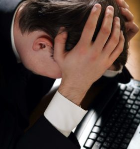 grieving employee at computer with head in hands