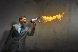 Young manager screaming furiously in megaphone that is shooting flames to illustrate wacky boss behavior post.