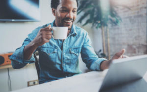 Black man drinking coffee while reading HR news on his laptop