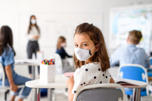 teacher with mask at front of a class for children who are back to school
