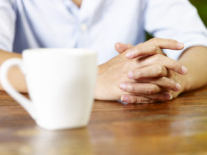closeup of coffee cup and tightly clasped hands depicting stress