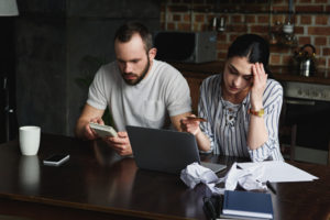 couple at home doing bills on their computer and showing signs of financial stress