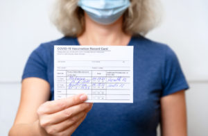 woman ib blue holding a vaccination record for proof in vaccine mandate