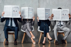 four seated professional people with open newspapers - turned to HR Web Cafe News, maybe
