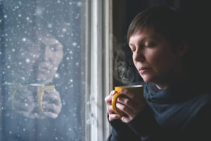 seasonal affective disorder - sad woman with a coffee cup, her face reflected in a snow encrusted window