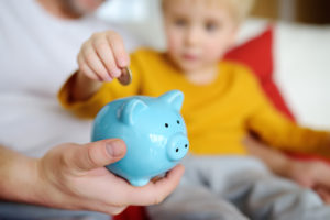 cute toddler with Dad putting coins in a piggy bank demonstrating that financial literacy should start early