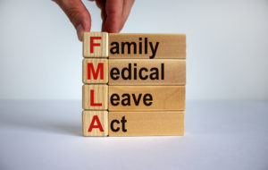 Hand stacking wooden blocks that spell out "FMLA - Family Medical Leave Act" to illustrate FMLA Update blog post