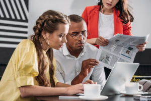 two women and a man reading news from laptops and newspapers over cover to illustrate HR news roundup