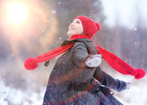 A happy girl twirling in the winter snow, She is in a grey coat with a red hat and red scarf that ishows motion. The image is selected to represent the February dates & events.