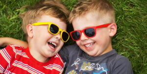 two cute small boys in sunglasses laying in the grass.