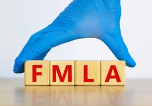 Blue gloved hand of an MD spells out the letters FMLA in blocks to illustrate FMLA update.