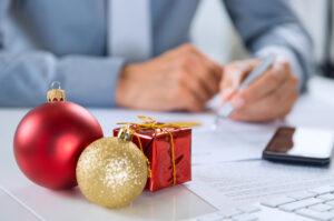 red and gold holiday ornaments on a desk, with a partial view of a man handling paperwork.