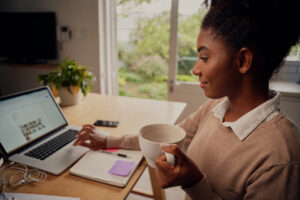 Young black professional woman drinking coffee while reading HR News Roundup on a laptop