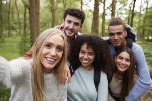 Multi ethnic group of five young adult friends taking a selfie in a forest during a hike to illustrate sober curious post
