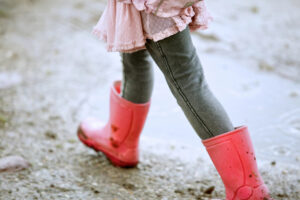 A little girl's legs clad in jeans and tall red boots splashing through puddles to illustrate key April dates posting.