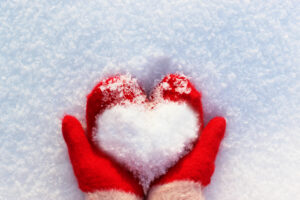 Human hands in warm red mittens with a snowy heart on a background of snow to illustrate key February dates blog post.