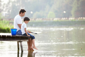 Father and young son sitting on a dock fishing to illustrate men's health month and father's day post of key June dates