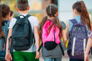 Three schoolkids walking to school wearing backpacks to illustrate blog post on August key events and dates.